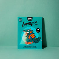 Boîte DIY Lamp 3D Dino OMY : lampe dinosaure en carton à monter, LED incluse, sur fond vert d'eau