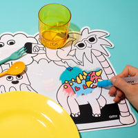 Main coloriant au feutre le set de table Magic Set Dino OMY, dinosaures à colorier, avec assiette, verre et couverts