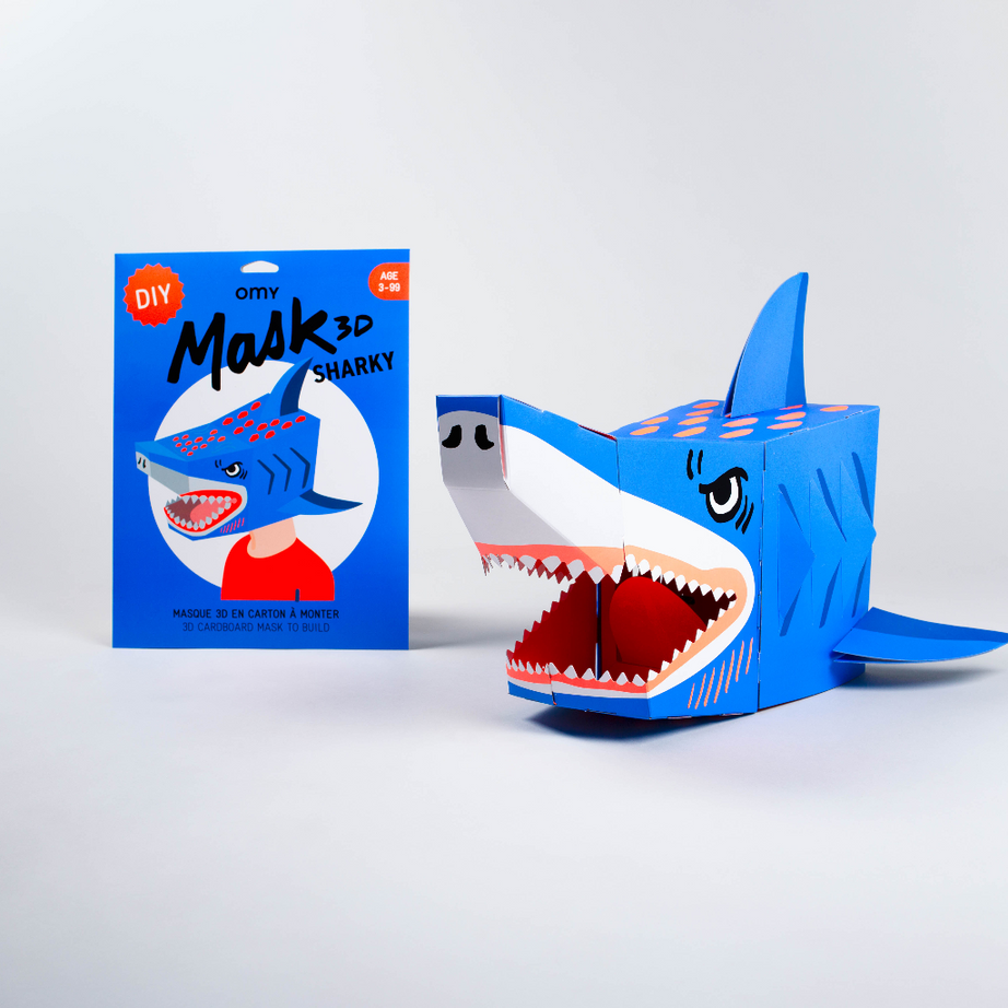 OMY Sharky DIY 3D-Maske: blaue Pappmaske eines Hais zum Zusammenbauen, zusammengebaut neben ihrer Tasche, auf weißem Hintergrund