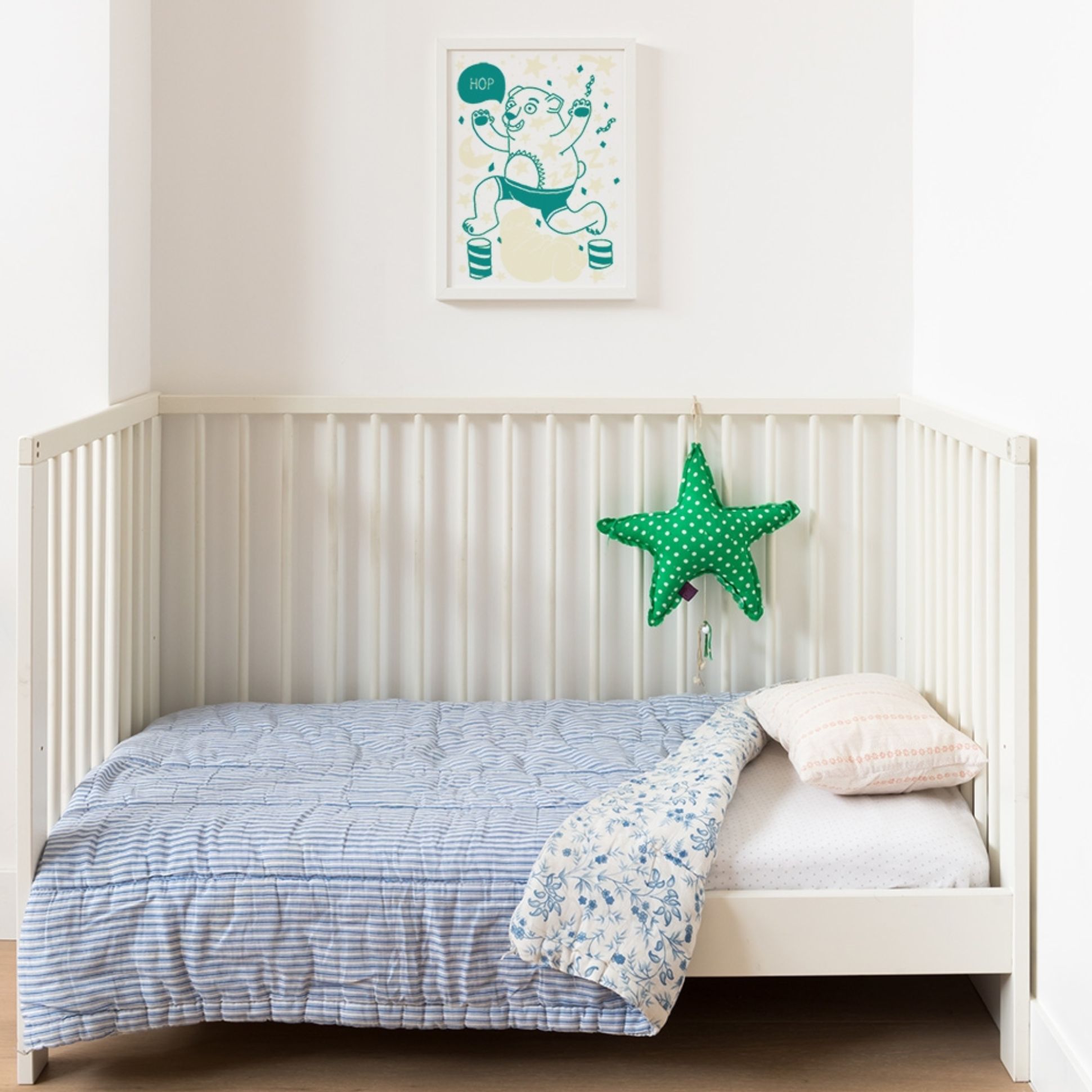 Chambre d'enfant : affiche OMY ourson « Hop » vert encadrée au-dessus d'un lit à barreaux blanc avec coussin étoile verte