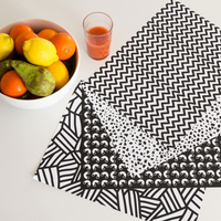 OMY Graphic.01 papieren placemats met 4 zwart-witte patronen op een tafel, met een fruitschaal en een sap