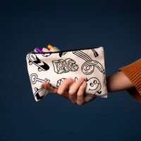 Hand holding the OMY coloring pouch in raw canvas with black-and-white motifs, markers sticking out, on a midnight blue background