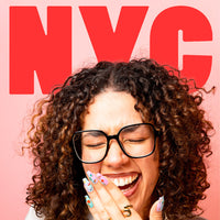 Laughing woman with glasses and curly hair, pastel nails decorated with OMY NYC nail stickers, red NYC letters.