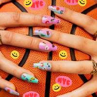 Long pastel nails decorated with OMY NYC nail stickers (taxi, pretzel, donut) on a basketball with smileys.