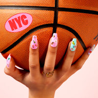 Hand with long pastel nails decorated with OMY NYC nail stickers holding a basketball with an NYC sticker.