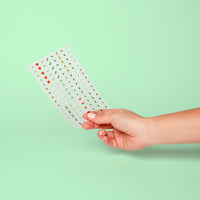 Stickervel met Paris OMY-nagelstickers in de hand: rode hartjes, lippen en kleine Parijse motieven, op een mintgroene achtergrond.