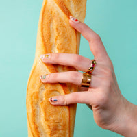 Hand met nagels versierd met Paris OMY-nagelstickers, houdt een stokbrood vast, op een turquoise achtergrond.