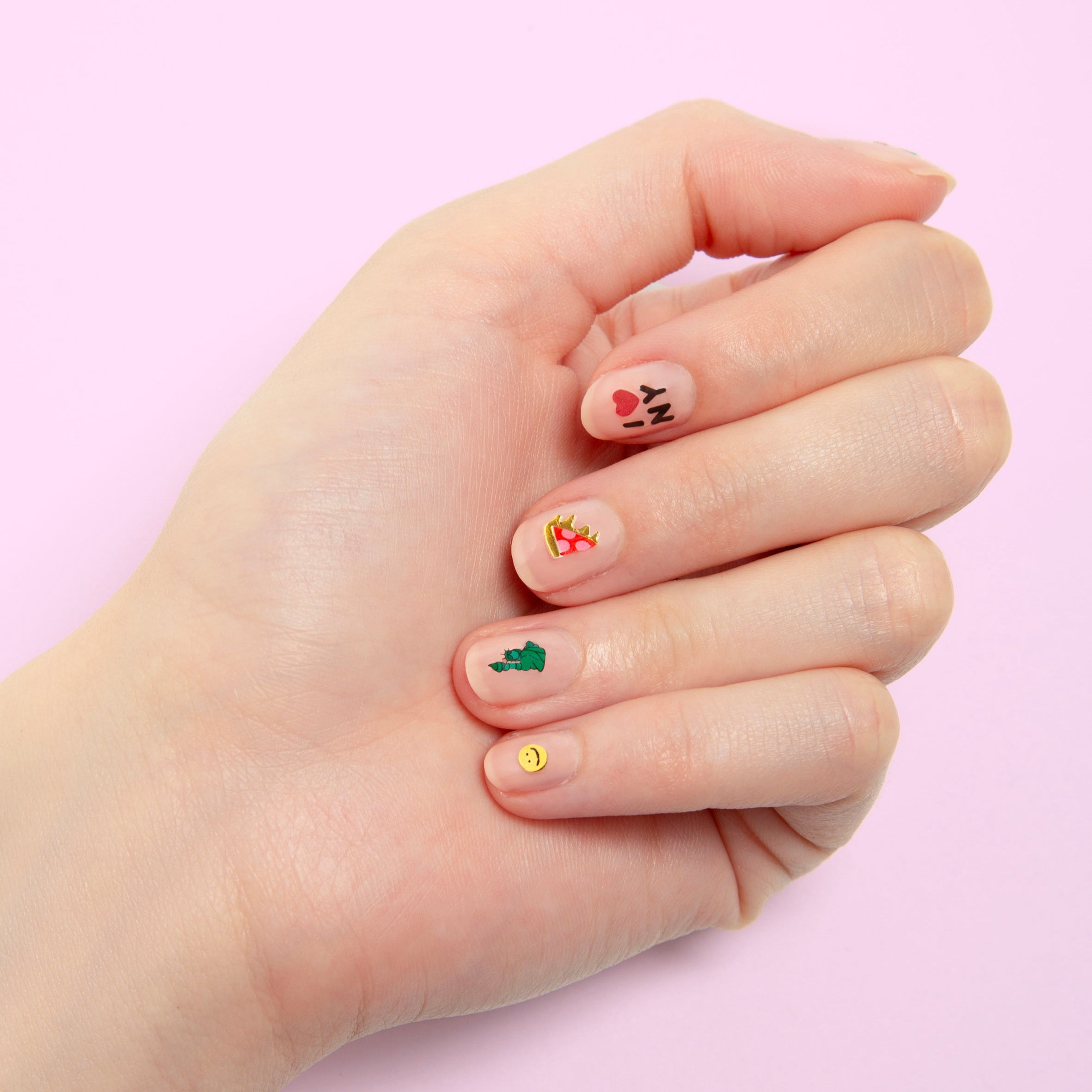 Hand with nude nails decorated with OMY NYC nail stickers: I love NY, Statue of Liberty and smiley, on a pink background.