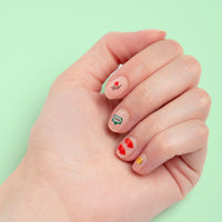 Hand met nude nagels versierd met Paris OMY-nagelstickers: Eiffeltoren, Paris-bord en rode hartjes, op een mintgroene achtergrond.