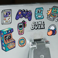 Détail des stickers Game Boy OMY holographiques avec consoles, manettes et texte Game Over