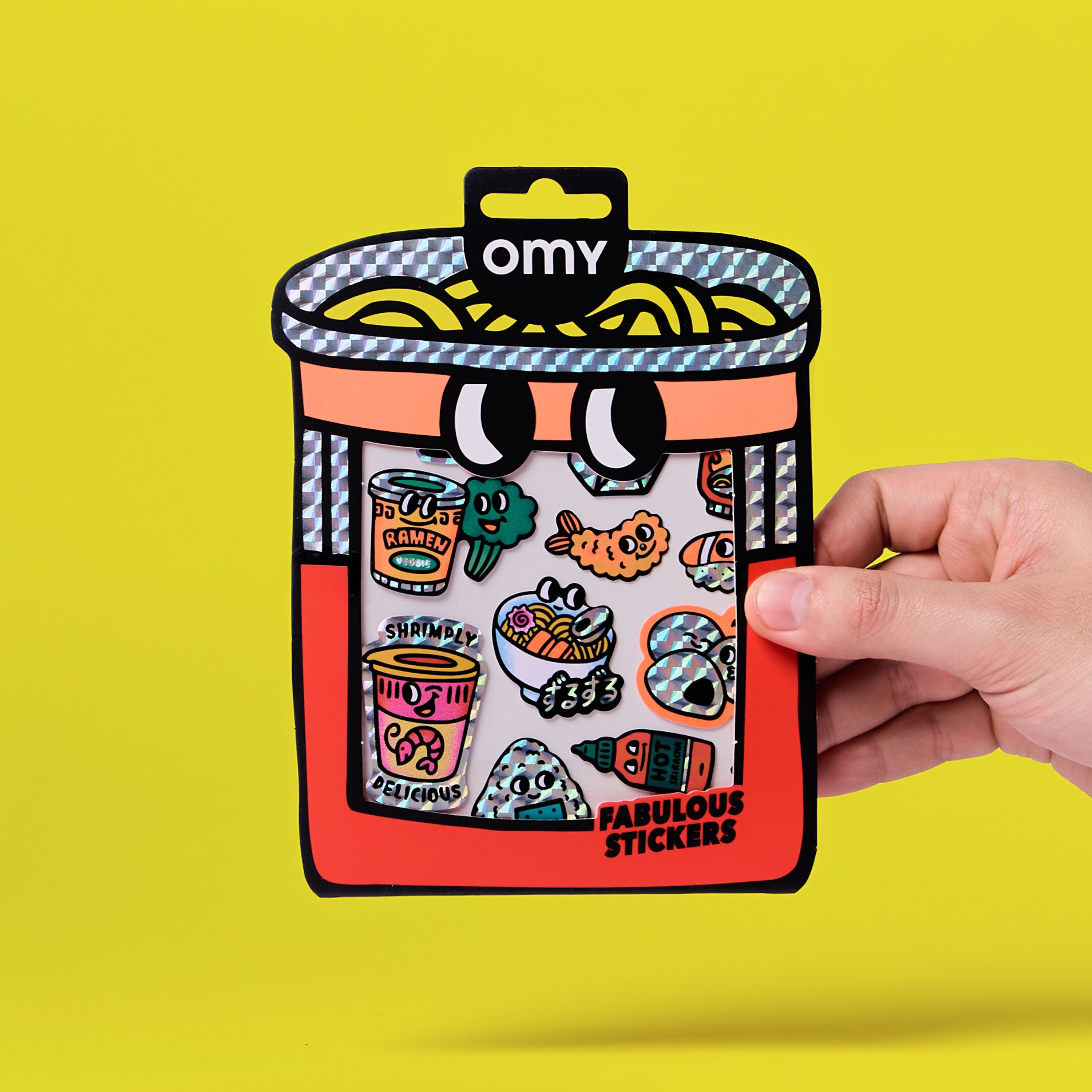 Fabulous Stickers Noodle OMY – planche de stickers ramen holographiques et fluorescents dans un packaging illustré, tenue en main sur fond jaune