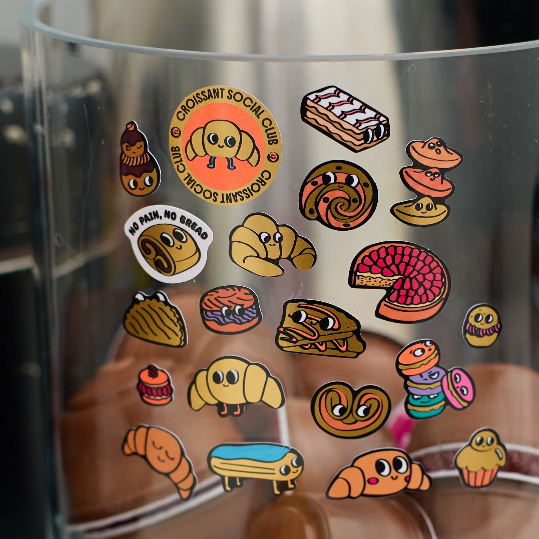 Croissant OMY pastry stickers stuck on a clear jar, croissant, pain au chocolat and bakery treat patterns.