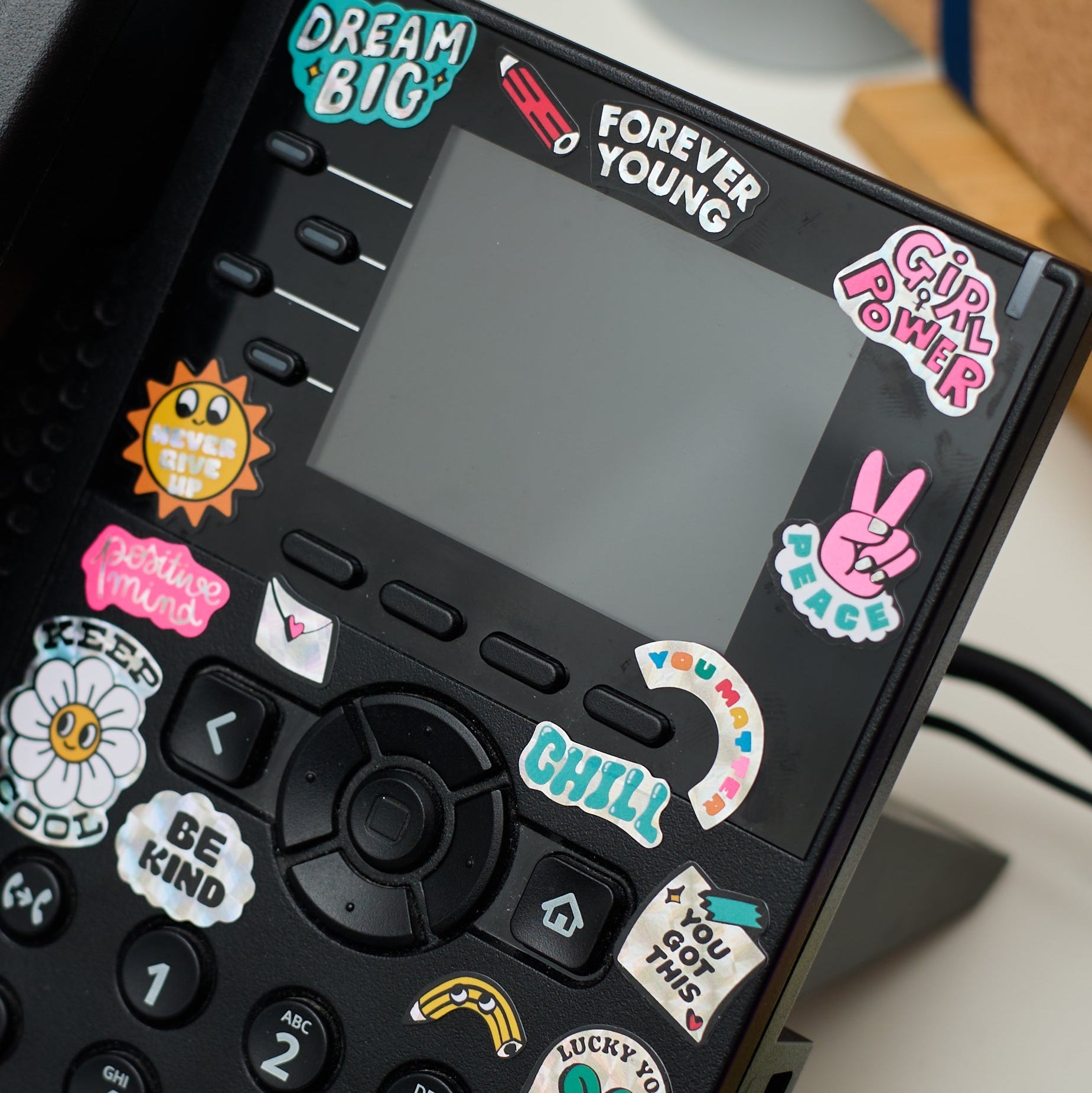 Holographic positive-message stickers by OMY stuck on a phone, inspiring words and colorful symbols