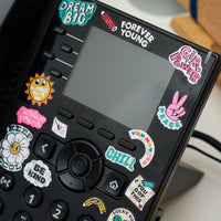 Holographic positive-message stickers by OMY stuck on a phone, inspiring words and colorful symbols