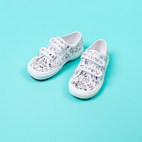 Pair of kids' Superga x OMY velcro sneakers with black-and-white illustrations to color, on a turquoise background