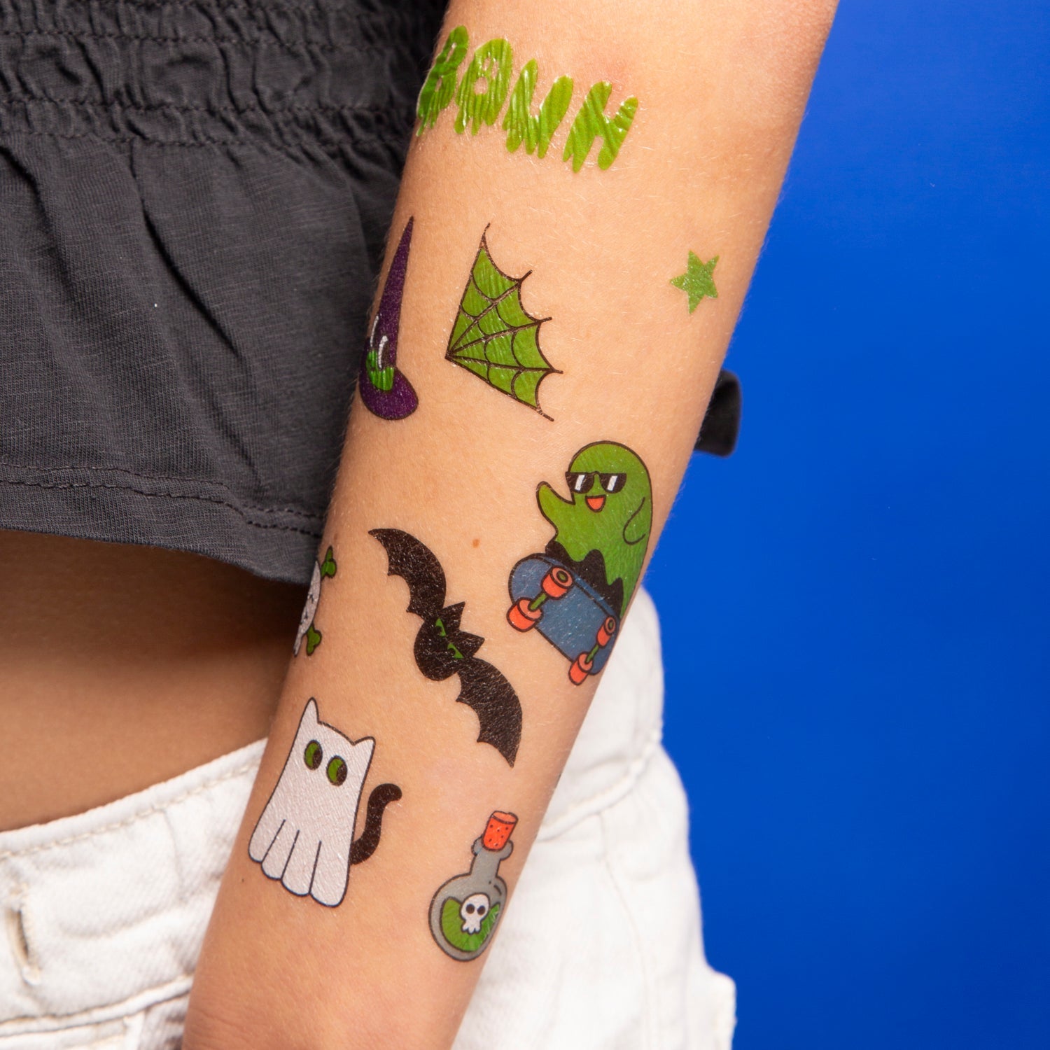 Avant-bras orné de tatouages éphémères phosphorescents Glow in the Dark OMY : fantôme en skate, chauve-souris, toile d'araignée et chat fantôme