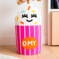 Tidy Bag - Yummy, pink and white striped felt storage basket shaped like a cupcake, ideal for toys and books, placed in a child's bedroom.