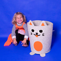 Tidy Bag OMY, panier de rangement en feutrine grise en forme de chat, à côté d'une petite fille souriante assise