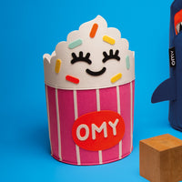 Tidy Bag - Yummy, felt storage basket shaped like a pink and white striped cupcake with colorful decorations and OMY logo.