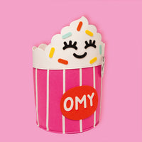 Tidy Bag - Yummy, kids' felt storage basket shaped like a pink and white cupcake with a smiling face and OMY logo, on a pink background.