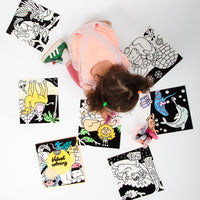 Top view of a little girl surrounded by Velvet Coloring Animals OMY pictures to color: lion, dolphin, giraffe and polar bear