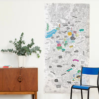 Coloriage géant XXL Brooklyn OMY affiché au mur dans un salon, carte de Brooklyn en partie coloriée, à côté d'un buffet et d'une chaise bleue