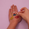 Vidéo d'application des tatouages éphémères Dinos OMY sur une main : dinosaure doré, volcan et bulle Grrr