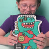 Vidéo d'une fille souriante présentant le Sticker Activity Book Dino OMY, carnet à stickers à spirale en forme de dinosaure turquoise